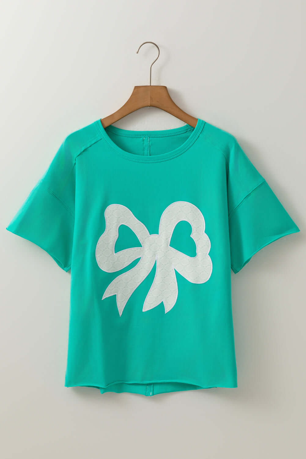 Teal Ribbon Theory Top with lace bow design and raw edge trim hanging on a wooden hanger.