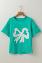 Teal Ribbon Theory Top with lace bow design and raw edge trim hanging on a wooden hanger.