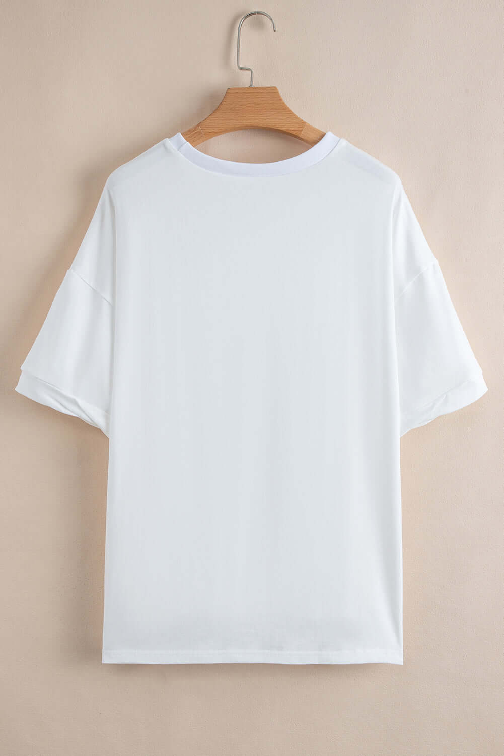 Back view of a white drop-shoulder t-shirt on a wooden hanger against a neutral background.