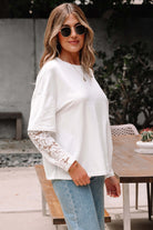 Woman in white Laced Logic Top with lace sleeves, stylishly posing outdoors with sunglasses.