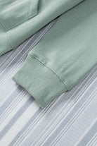 Close-up of teal hoodie sleeve with ribbed cuff on a striped background.