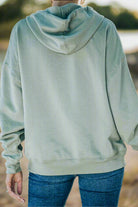 Vivian-Lu LIVING IT UP Hoodie in sage green with fleece lining and contrast band detail, shown from the back outdoors.