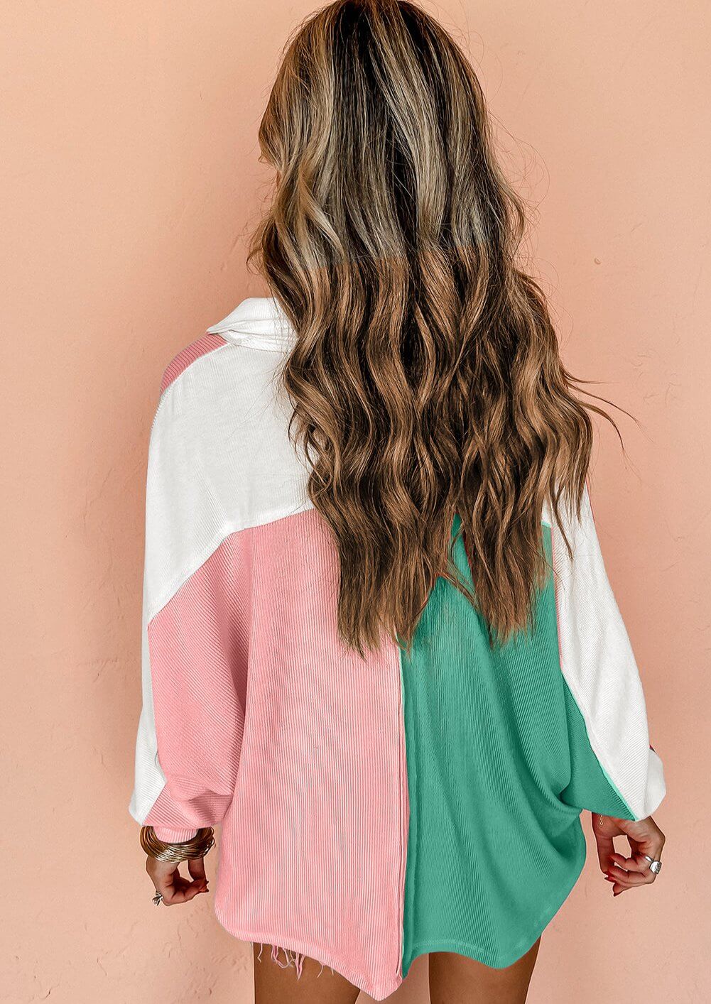 Woman wearing oversized top with pink, green, and white color block pattern, featuring buttoned neckline, relaxed fit, and long, wavy hair.