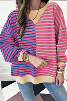 Color block striped sweatshirt with drop shoulders, featuring pink and navy tones, styled casually with bracelets and jeans.