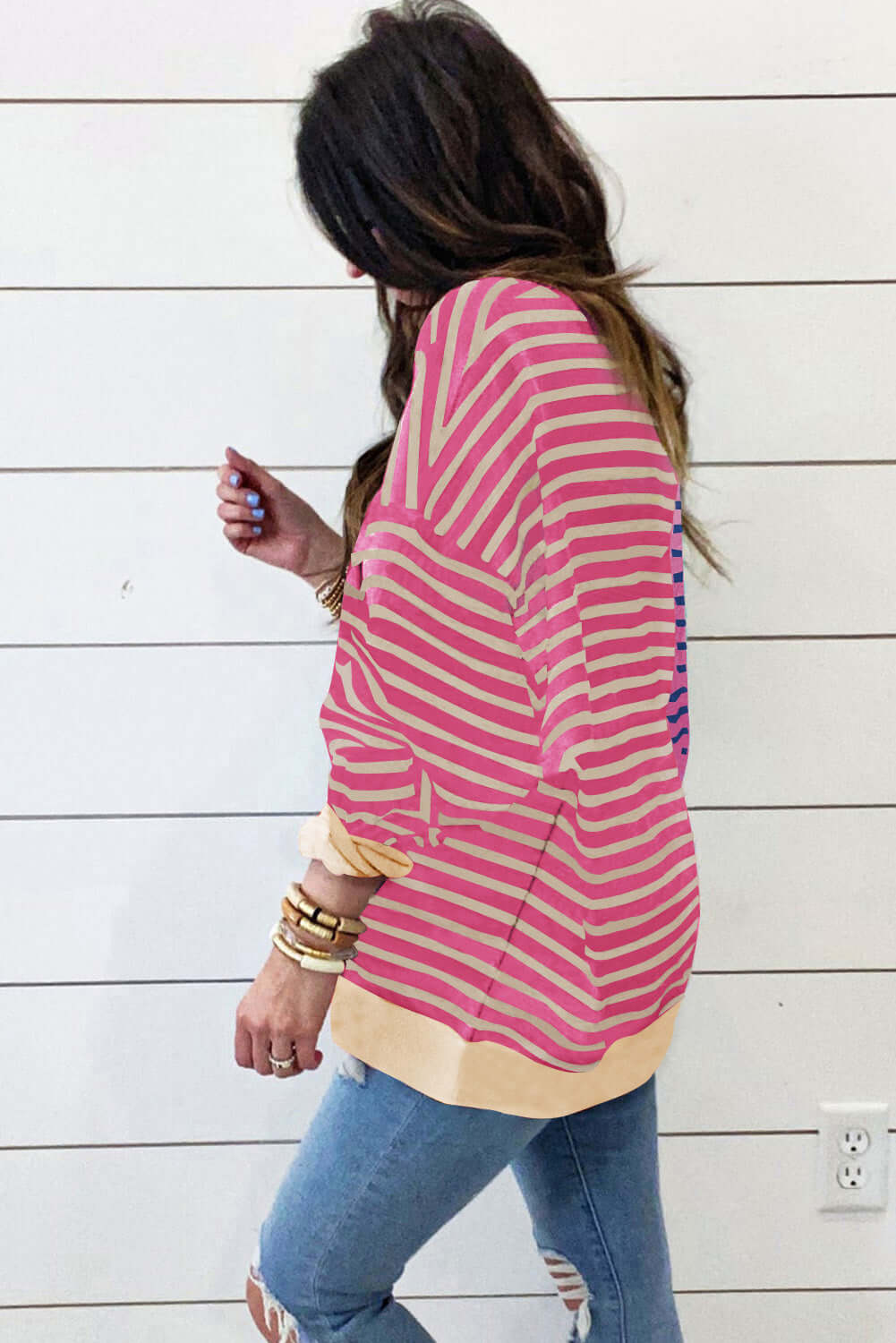 Woman wearing an oversized pink and cream striped sweatshirt, showcasing a relaxed style and drop shoulder design.