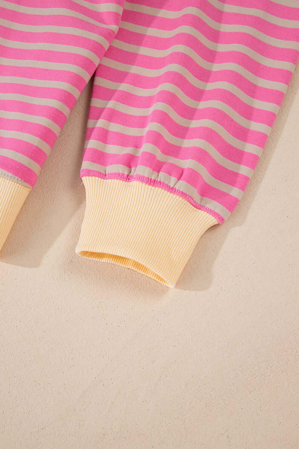 Close-up of pink and beige striped sweatshirt cuffs showcasing a relaxed, oversized style with drop shoulder design.