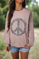 Woman wearing INNER PEACE sweatshirt with floral peace symbol design, drop shoulder, and long sleeves in a casual outdoor setting.