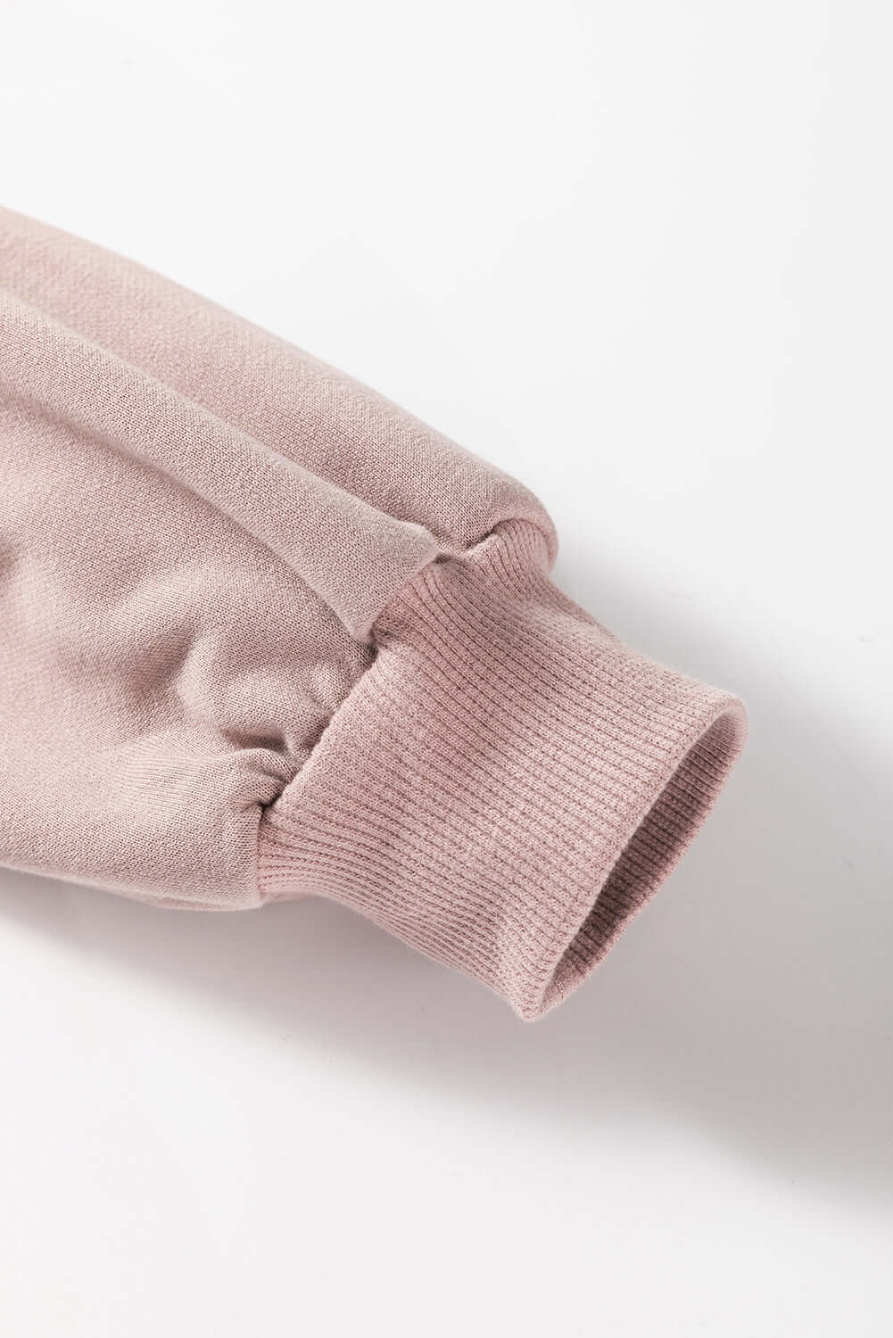 Close-up of pink sweatshirt sleeve, featuring ribbed cuff and drop shoulder design, made of cozy polyester-cotton blend fabric.