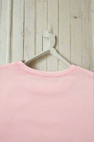 Light pink sweatshirt on a hanger against wooden background, featuring ribbed neckline detailing.