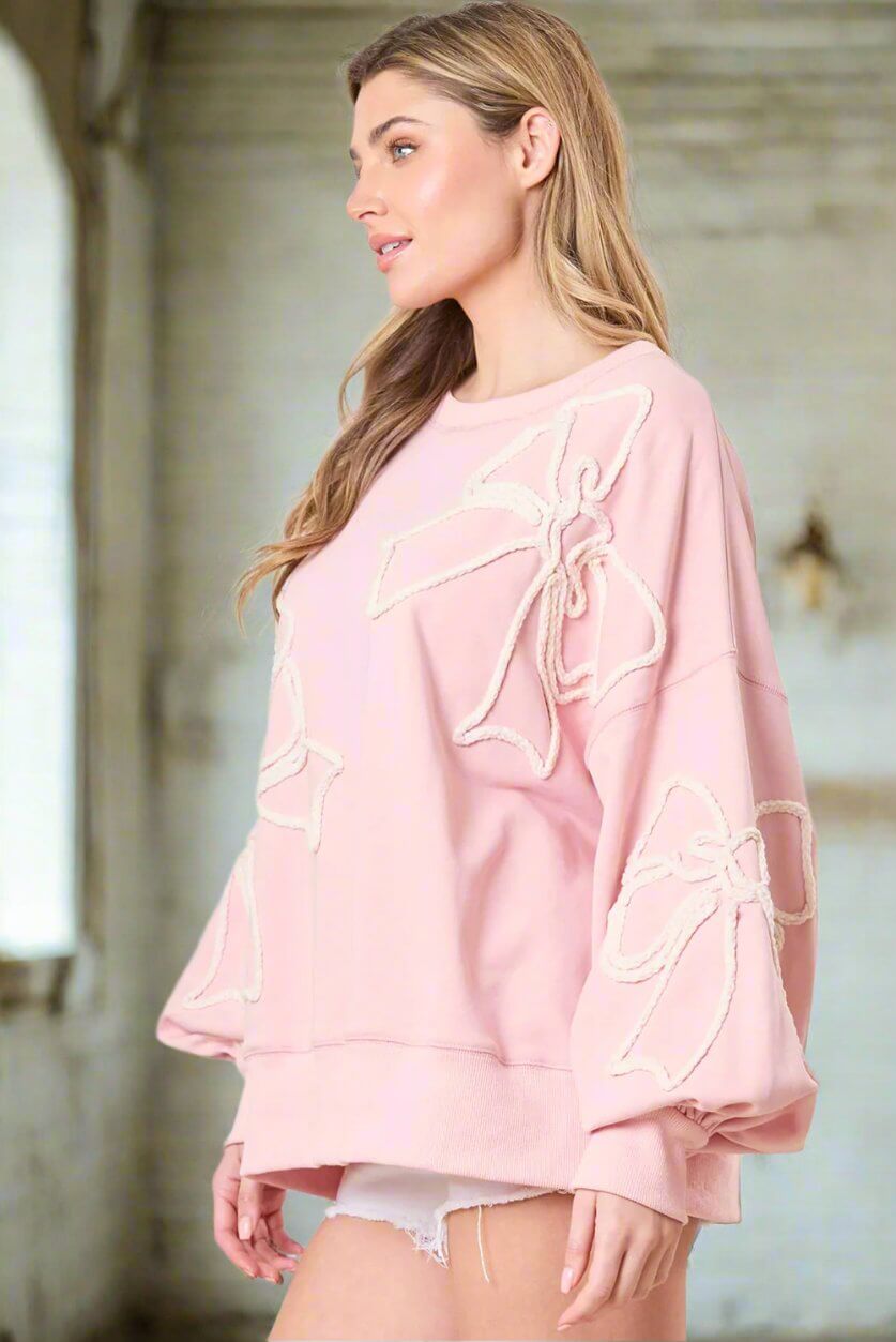 Vivian-Lu light pink sweatshirt with off white bow embroidery, ribbed edges, modeled by a woman, perfect for casual style.