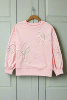 Light pink sweatshirt with white bow embroidery by Vivian-Lu, featuring ribbed edges, hanging on wooden hanger against white backdrop.