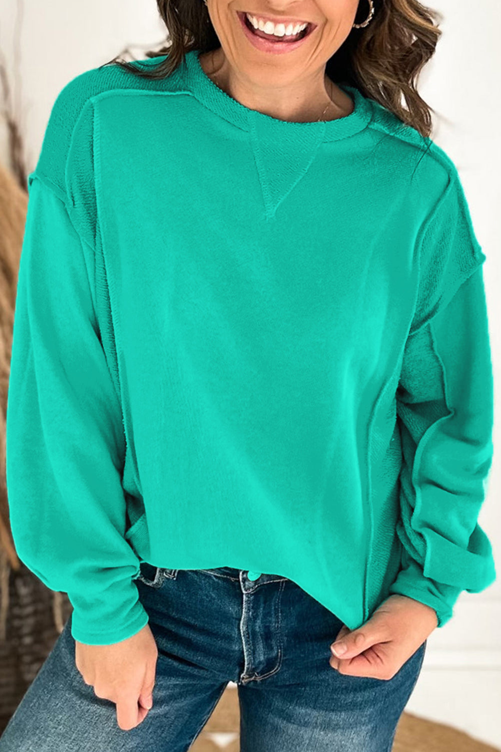 Woman wearing a teal crewneck sweatshirt with relaxed fit and splicing details, styled casually with jeans.