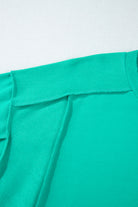 Close-up of teal crewneck sweatshirt showcasing sleek splicing details and structured design.