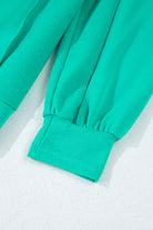 Close-up of teal crewneck sweatshirt sleeves showcasing ribbed cuffs and sleek fabric texture.