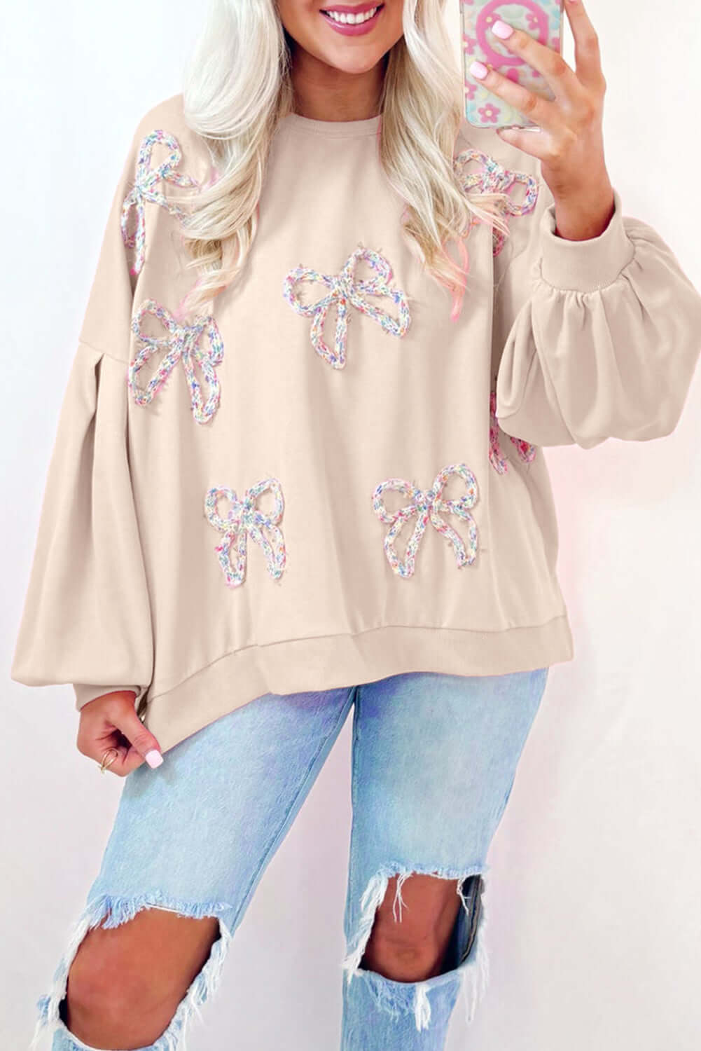 Beige Bowtique Top with embroidered bows and lantern sleeves, styled with distressed jeans.