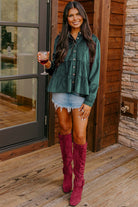 Woman wearing forest green State of Grace top with ruffle tiers, holding a drink, styled with denim shorts and red boots.