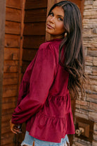 Woman wearing burgundy State of Grace top with ruffle tiers and O neck collar, styled with denim shorts, standing outdoors.