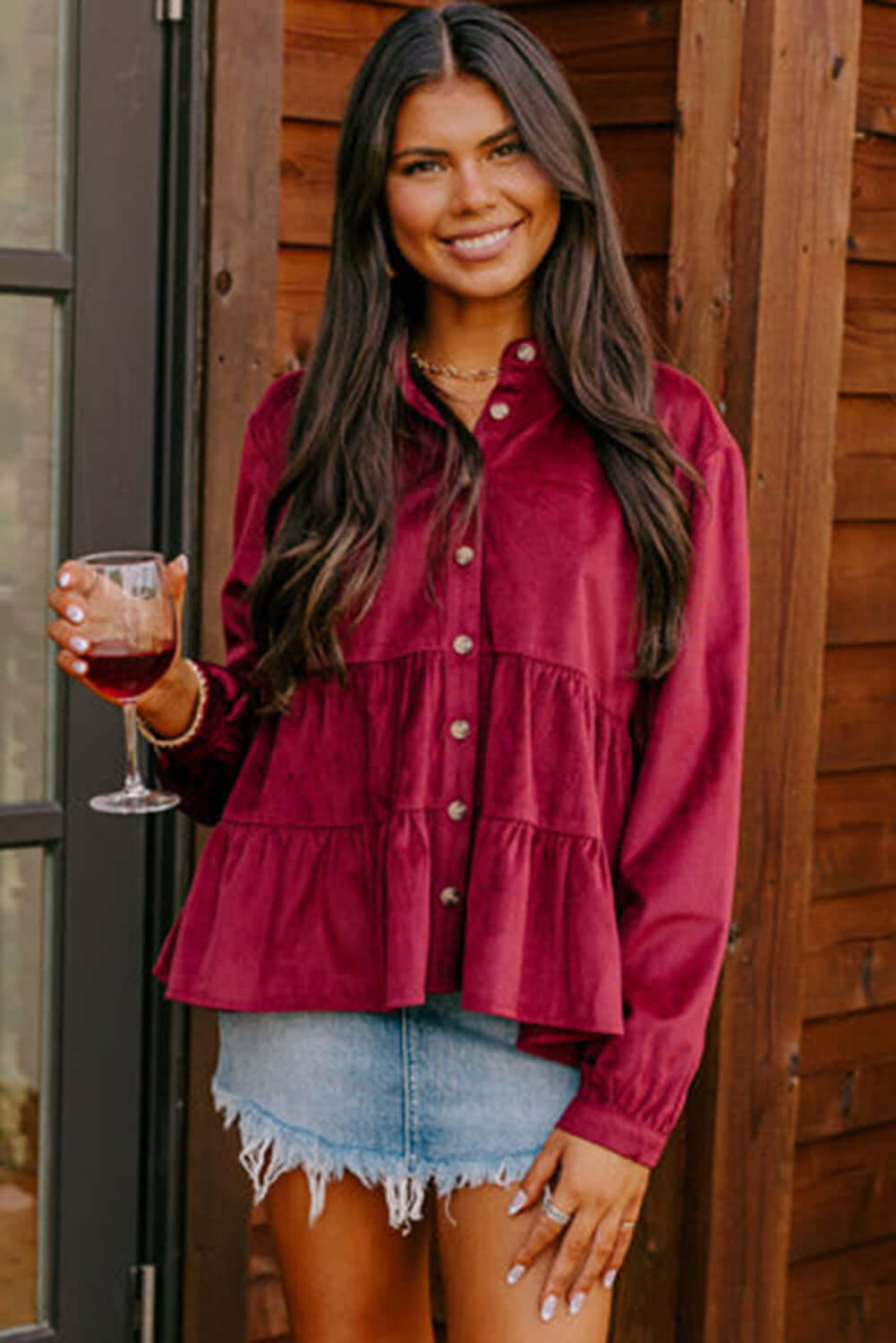 Woman wearing State of Grace top in burgundy with ruffle tiers and button-up style, paired with denim skirt, holding a glass of wine.