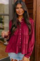 Woman wearing burgundy Vivian-Lu State of Grace top with ruffle tiers and button-up style, holding a glass of wine.