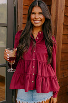 Woman wearing Vivian-Lu burgundy State of Grace top, ruffle tiered design, button-up style, holding a glass of wine.