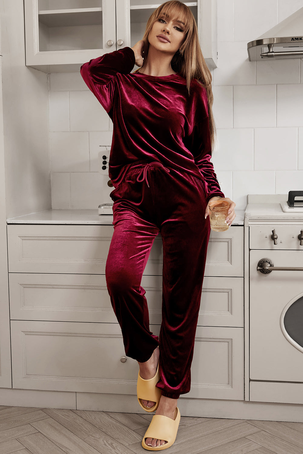 Woman wearing velvet wine two-piece set with long sleeve top and drawstring pants, standing in a modern kitchen.