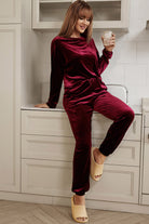 Woman in burgundy velvet wine two-piece set with long sleeve top and drawstring pants, sitting in a stylish kitchen.