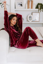 Woman lounging in a burgundy velvet two-piece set with long sleeves and drawstring pants, stylish and comfortable home outfit.