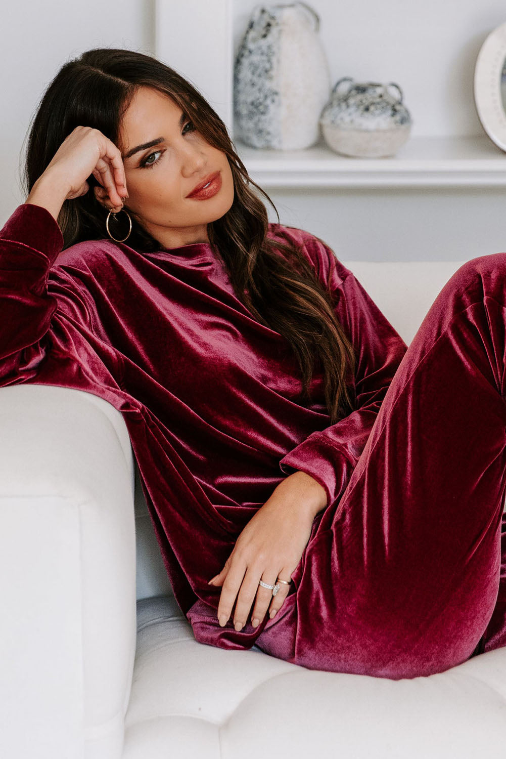 Woman wearing Velvet Wine set in burgundy, lounging on white sofa, showcasing trendy long sleeve top and drawstring pants.