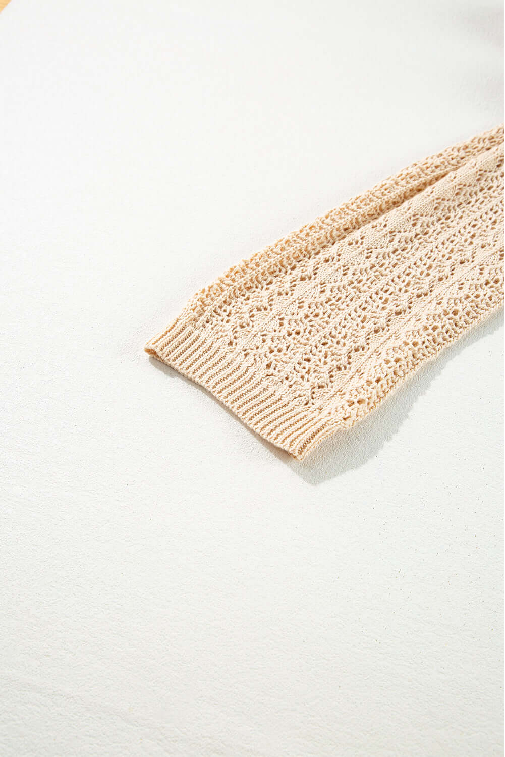 Close-up of the soft apricot beige cable knit sleeve of the Café Date Cardigan on a light background.