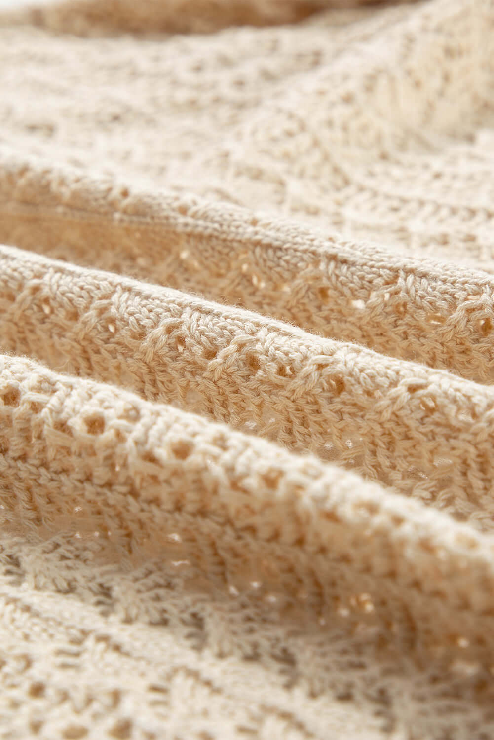 Close-up of intricate cable knit fabric in apricot beige, showcasing delicate hollow-out patterns.