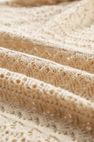 Close-up of intricate cable knit fabric in apricot beige, showcasing delicate hollow-out patterns.
