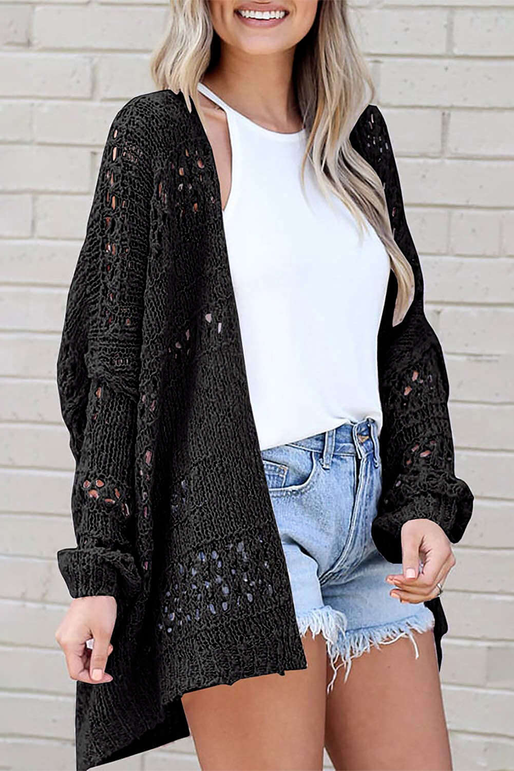 Stylish woman wearing a black cable-knit cardigan over a white top and shorts, perfect for breezy days.