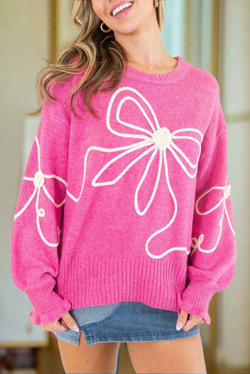 Soft pink sweater with corded bows, ruffled cuffs, and dropped shoulders, perfect for a trendy look and comfort.