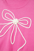 Pink sweater with white corded bow detail on the front, featuring ribbed neckline, perfect for trendy, comfortable style.