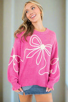 Soft pink sweater with corded bows and ruffled cuffs, worn by a smiling woman in a stylish casual outfit.