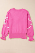 Soft pink sweater with corded bows, dropped shoulders, and ruffled cuffs; perfect for a trendy and cozy look.