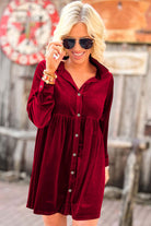 Woman wearing a vibrant velvet dress in berry red with a collared neck and front buttons, smiling outdoors.