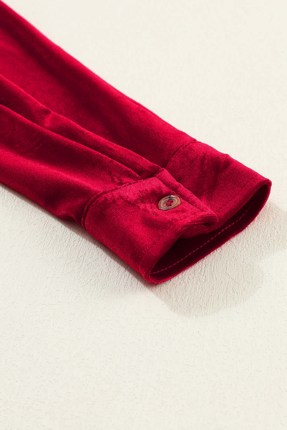 Close-up of a red berry velvet dress sleeve with button detail, showcasing the luxurious and textured fabric of the Vivian-Lu dress.