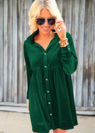 Woman wearing vibrant velvet emerald dress with buttons and collar, holding sunglasses, showcasing stylish outfit suitable for comfort and elegance.