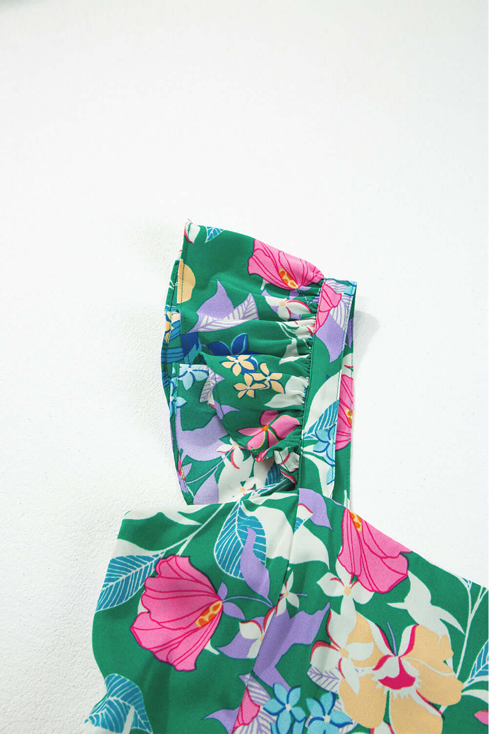 Close-up of a vibrant floral print dress featuring ruffles and green fabric, perfect for summer days.