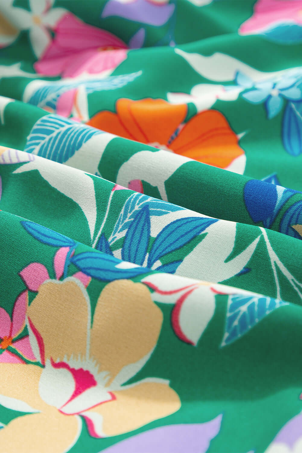 Close-up of vibrant floral fabric in green, featuring pink, orange, and blue blooms, perfect for a summer dress.