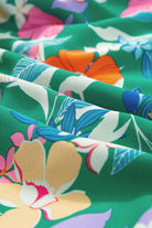 Close-up of vibrant floral fabric in green, featuring pink, orange, and blue blooms, perfect for a summer dress.