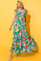 Vibrant green floral maxi dress with ruffles, perfect for summer days and twirling, model posing against a yellow background.
