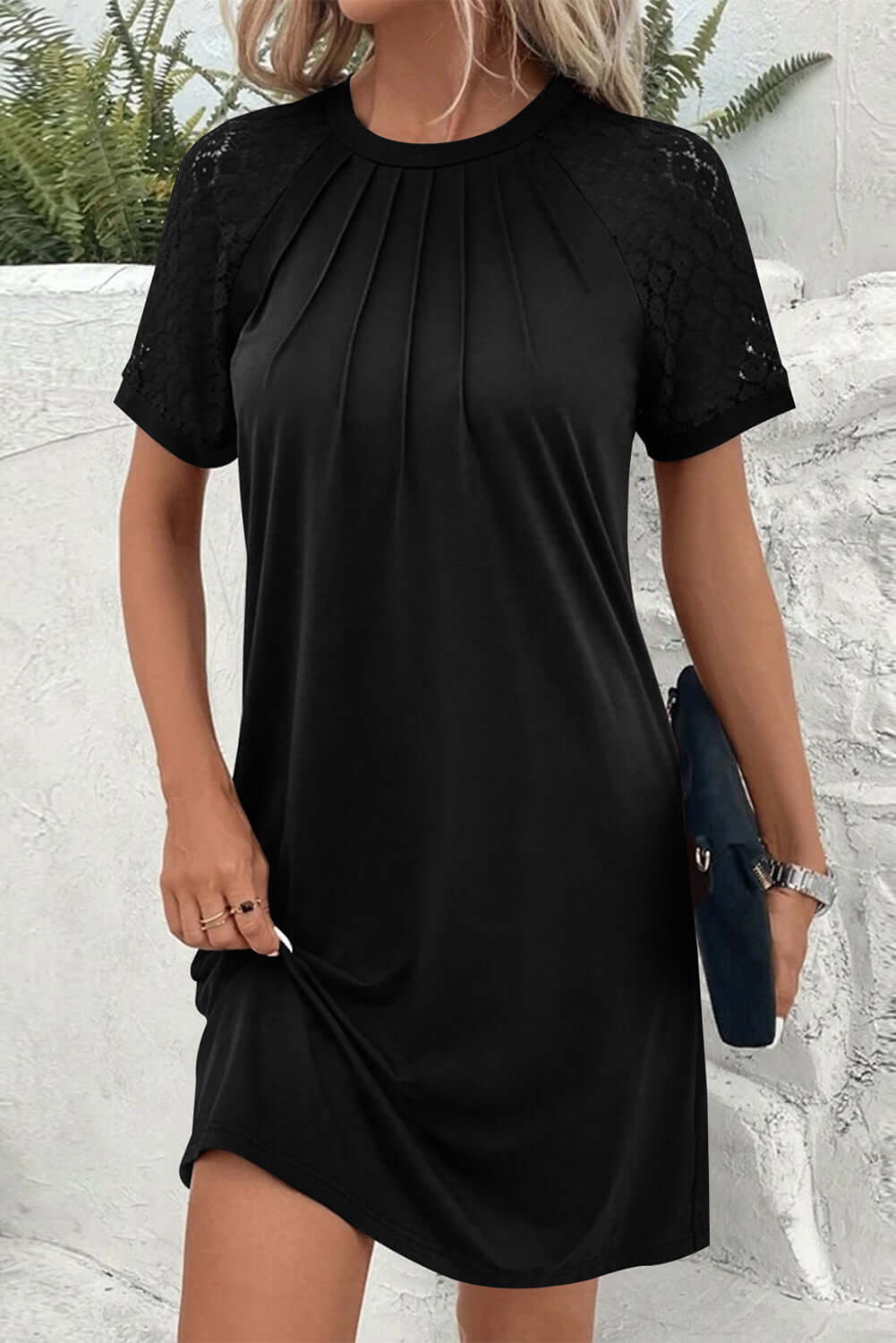 Woman wearing a chic black Shadow Luxe Dress with lace sleeves and pleated neckline for stylish comfort.