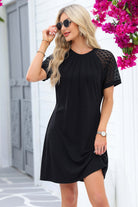 Chic black Shadow Luxe Dress with lace sleeves, pleated neckline, styled with sunglasses in a floral setting.