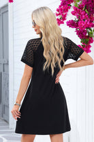 Model wearing a chic black Shadow Luxe Dress with lace sleeves against a floral backdrop.