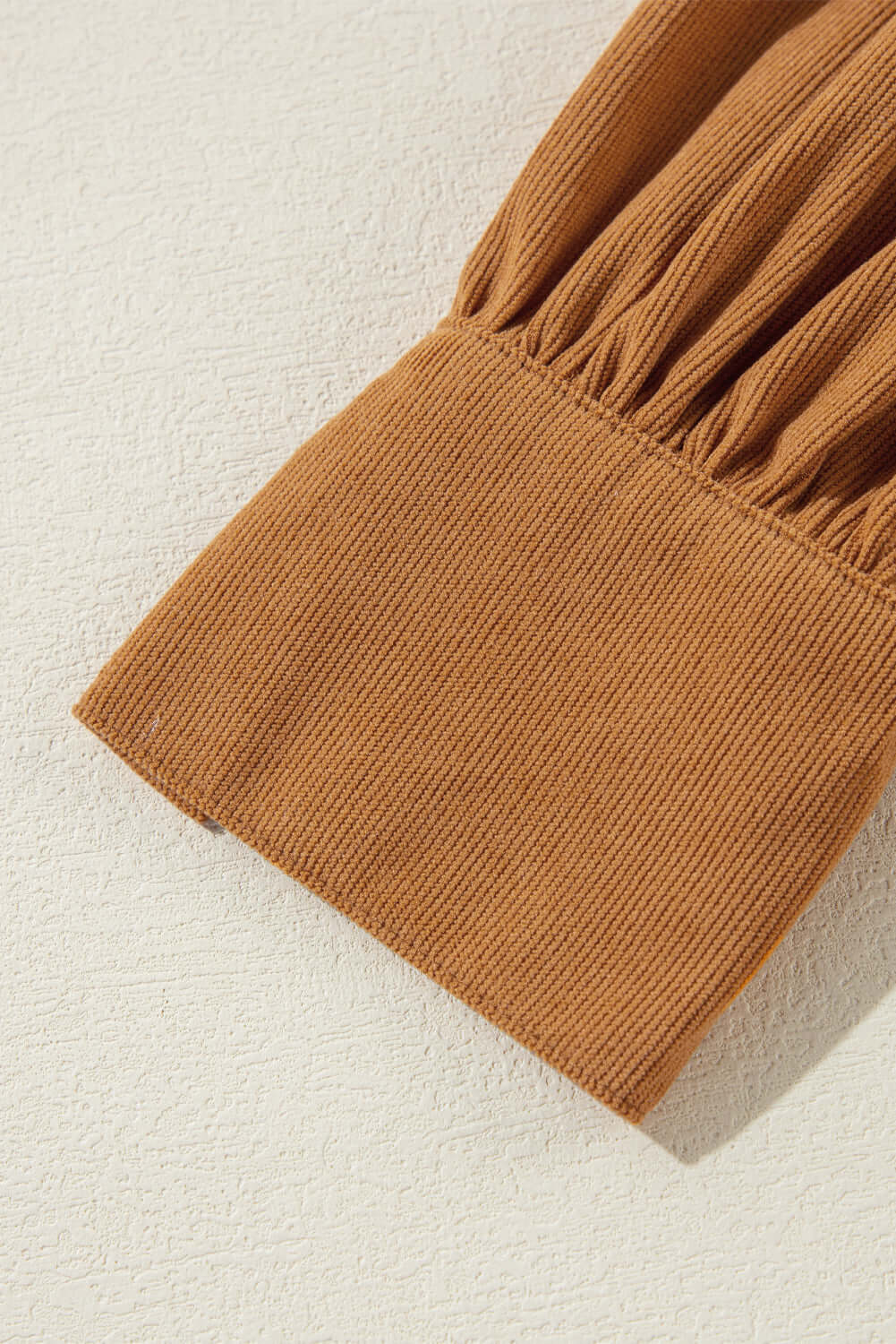 Close-up of copper-colored corduroy fabric with pleating and puff sleeve detail from DESERT WINDS Dress, showcasing luxury texture.