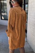 Woman wearing copper corduroy dress with puff sleeves and pleating, viewed from the back, showcasing elegant fall fashion.