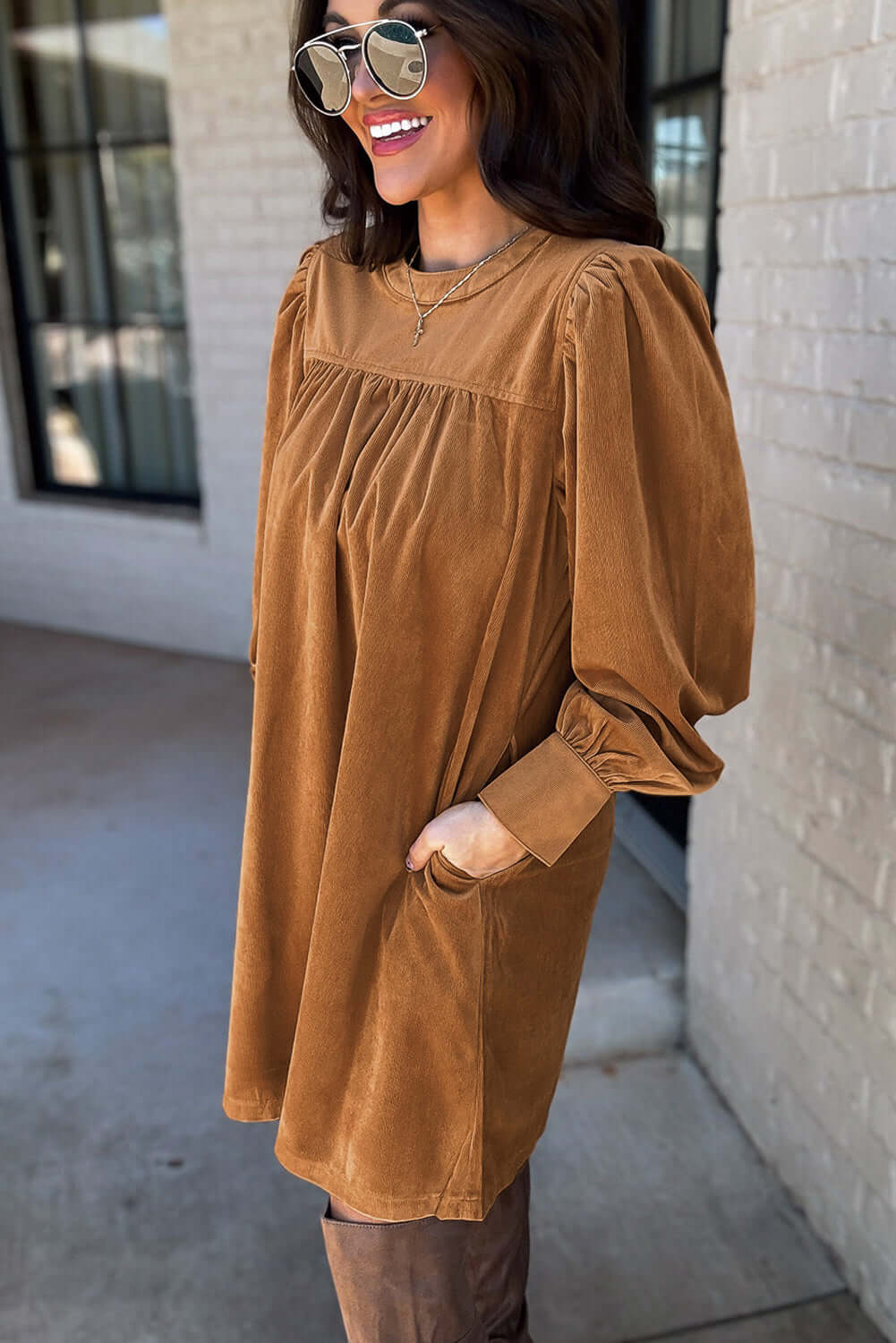 Woman wearing DESERT WINDS copper dress with puff sleeves and pleats, made of luxurious corduroy fabric, standing outside.