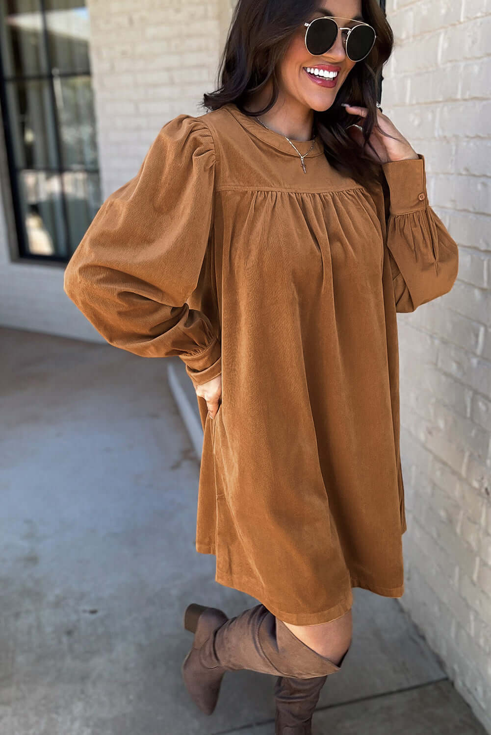 Woman in copper corduroy shift dress with puff sleeves, showcasing stylish pleating and a luxurious texture.